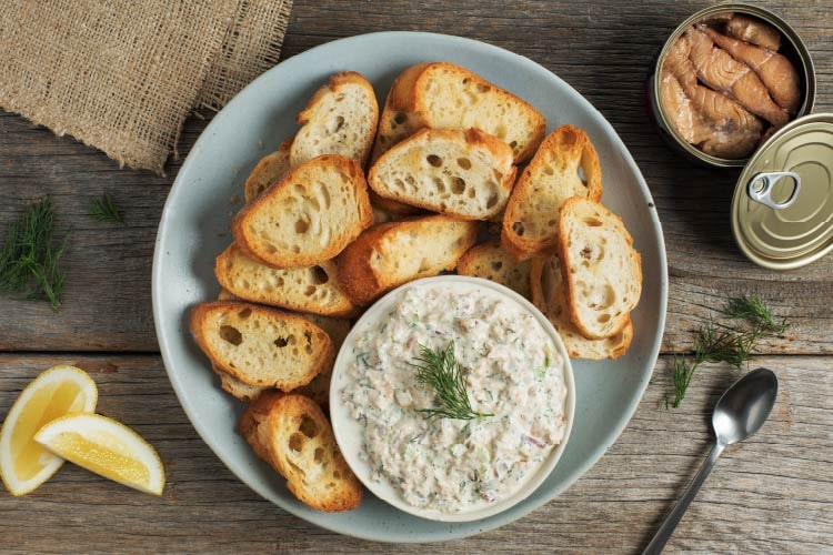 Top-down view of creamy Smoked Salmon Dip in a bowl, garnished with fresh dill sprigs, next to a freshly opened can of St. Jean's Smoked Pink Salmon - a delicious representation of West Coast Canadian cuisine.