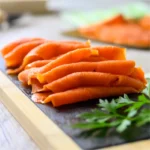 Image of thinly sliced cold smoked salmon lox arranged artistically on a dark slate charcuterie board. The salmon's rich, pinkish-orange color contrasts beautifully against the slate, enhancing its visual appeal. Sprigs of fresh, vibrant green parsley add a pop of color and texture, suggesting freshness and enhancing the overall aesthetic of the culinary presentation
